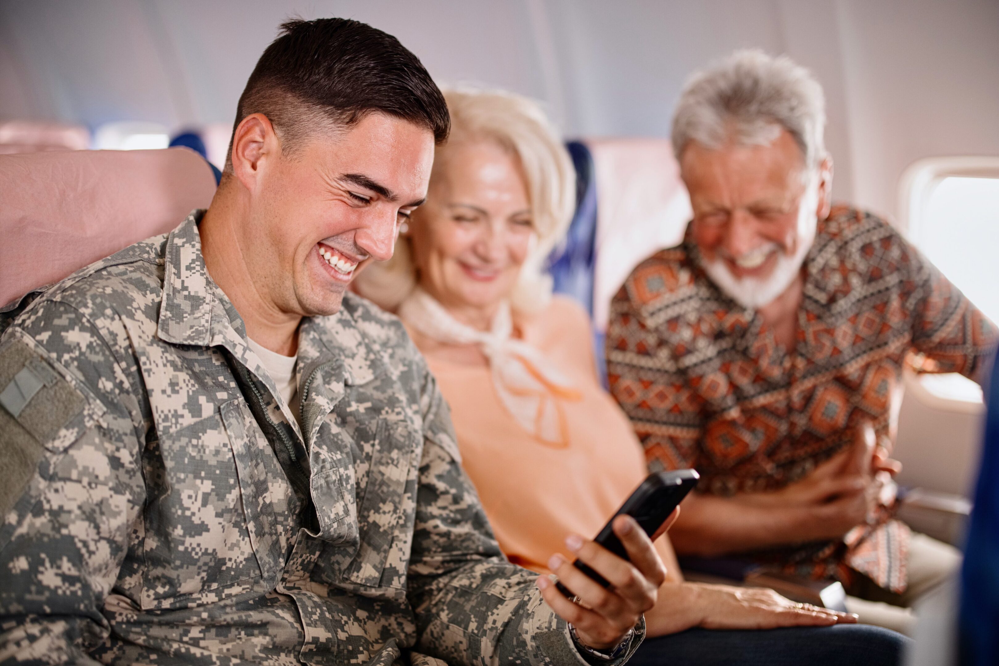 Soldier smiling with elderly couple on plane.